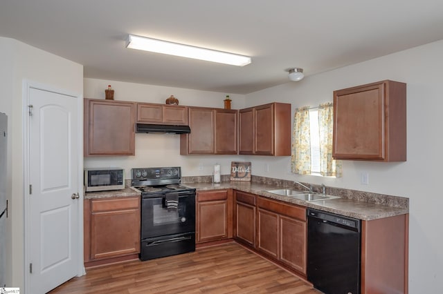 kitchen with light wood finished floors, dark countertops, a sink, under cabinet range hood, and black appliances