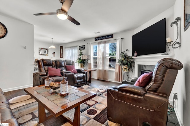 living area with a fireplace, visible vents, ceiling fan, wood finished floors, and baseboards