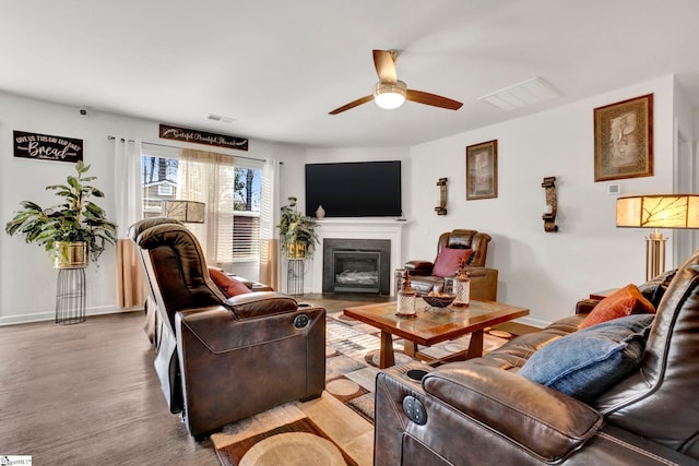 living room featuring a ceiling fan, a glass covered fireplace, visible vents, and baseboards