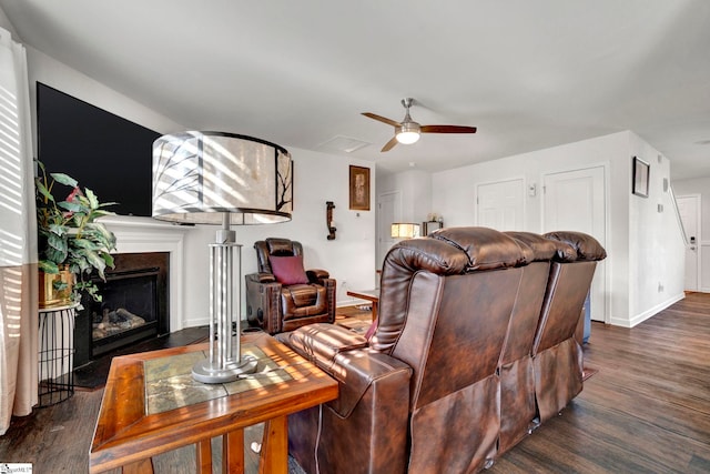 living area with a fireplace with flush hearth, dark wood finished floors, baseboards, and a ceiling fan