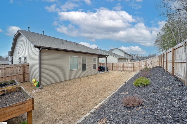 back of property with roof with shingles, a fenced backyard, and a garden