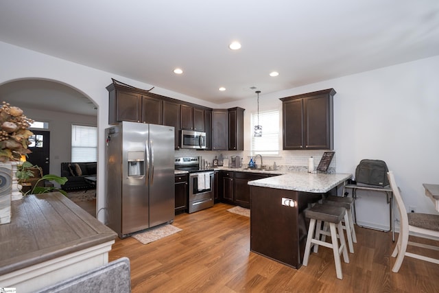 kitchen featuring arched walkways, a peninsula, appliances with stainless steel finishes, and dark brown cabinetry