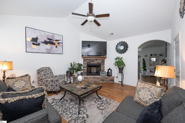 living area featuring arched walkways, lofted ceiling, visible vents, a stone fireplace, and wood finished floors