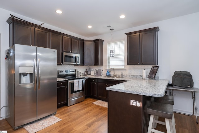 kitchen with a peninsula, stainless steel appliances, dark brown cabinets, light wood-type flooring, and a sink