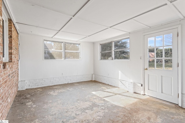 empty room with a paneled ceiling, brick wall, and concrete flooring