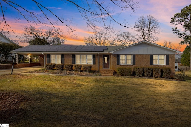 view of front of house with an attached carport, solar panels, brick siding, a lawn, and board and batten siding