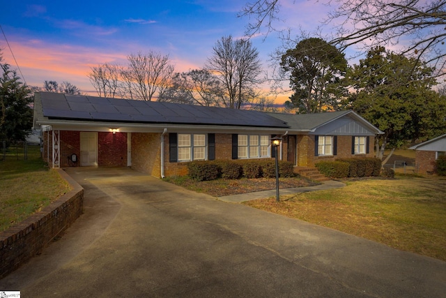 ranch-style house featuring solar panels, concrete driveway, an attached carport, a yard, and brick siding