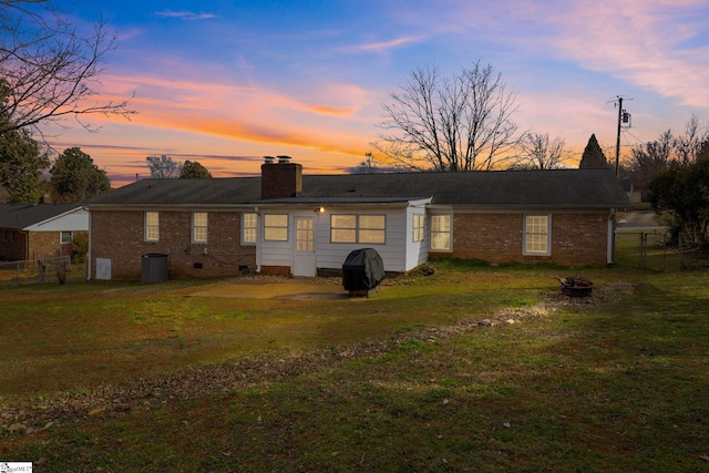 back of property featuring brick siding, a lawn, a chimney, and fence