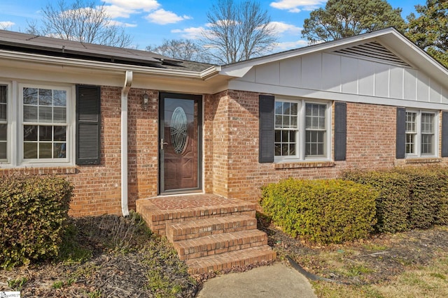 entrance to property featuring board and batten siding, solar panels, and brick siding