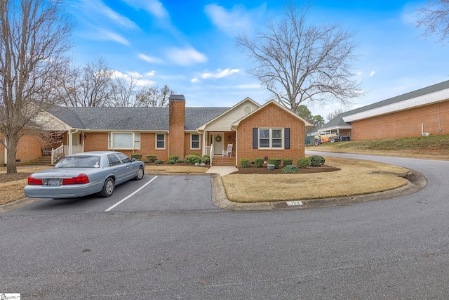 ranch-style home with a chimney, uncovered parking, and brick siding