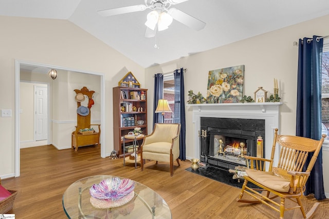 sitting room featuring baseboards, a ceiling fan, lofted ceiling, a fireplace with flush hearth, and wood finished floors