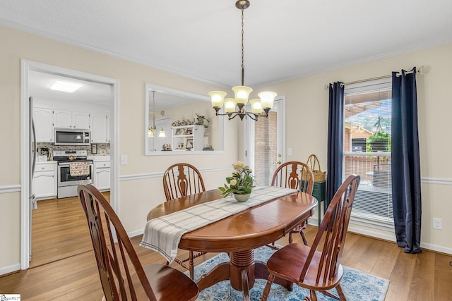 dining area with light wood-style floors, baseboards, ornamental molding, and a notable chandelier