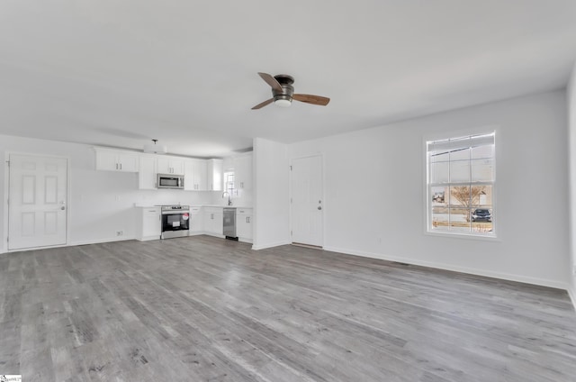 unfurnished living room with light wood-style floors, a sink, baseboards, and a ceiling fan