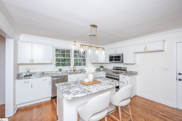 kitchen featuring light wood-type flooring, crown molding, stainless steel appliances, and a sink