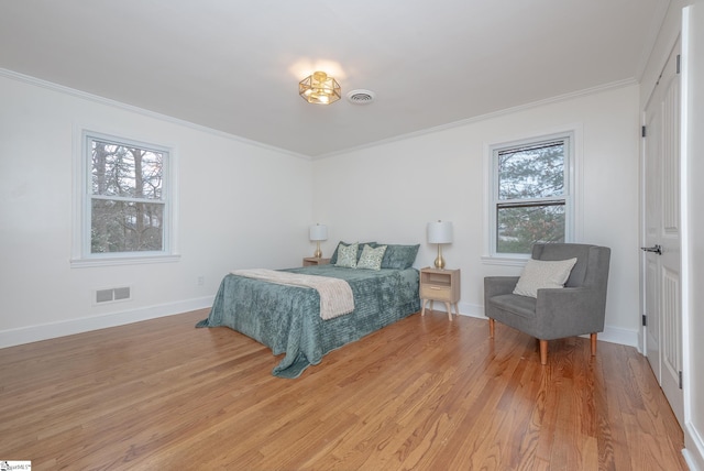 bedroom featuring light wood finished floors, baseboards, visible vents, and ornamental molding