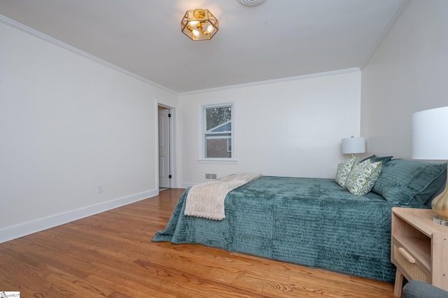 bedroom with crown molding, visible vents, baseboards, and wood finished floors