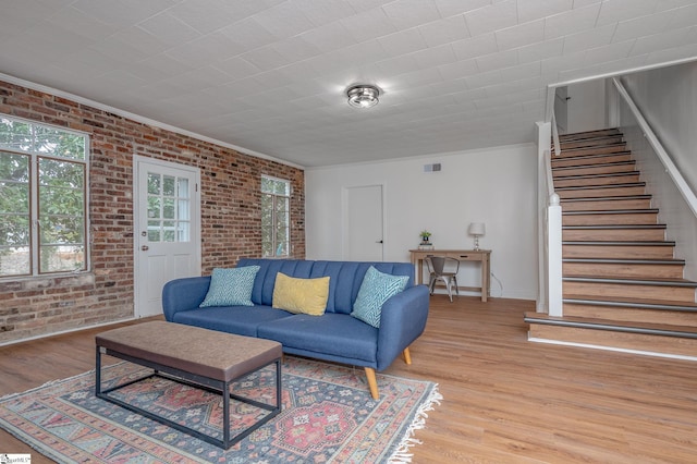 living room with brick wall, stairway, visible vents, and light wood-style floors