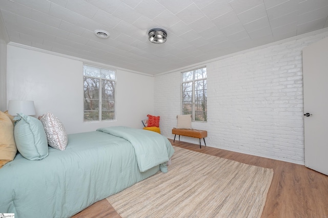 bedroom featuring brick wall, ornamental molding, multiple windows, and wood finished floors