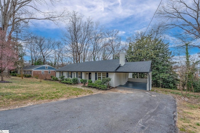 view of front of house featuring a shingled roof, a chimney, aphalt driveway, a front lawn, and a carport