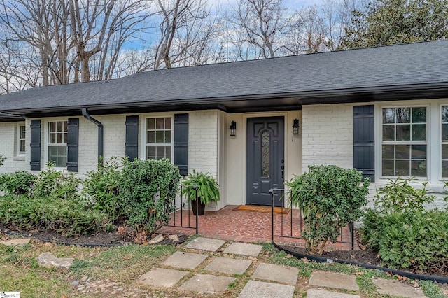 ranch-style house featuring brick siding and roof with shingles