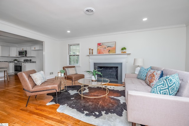 living area featuring a fireplace, visible vents, crown molding, and wood finished floors