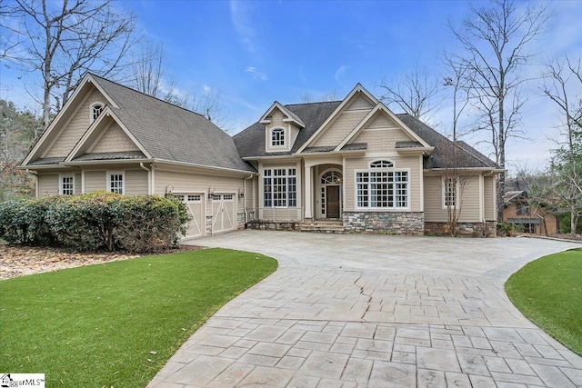 craftsman house with a garage, stone siding, a front lawn, and decorative driveway