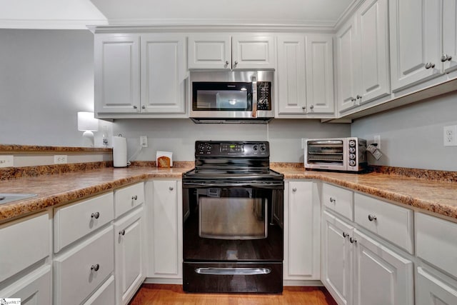 kitchen featuring a toaster, white cabinets, stainless steel microwave, black electric range, and light wood-style floors