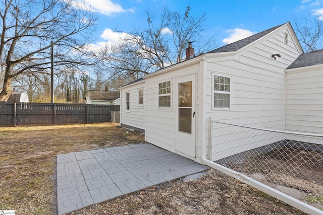 view of home's exterior with a patio area, a fenced backyard, a chimney, and a shingled roof