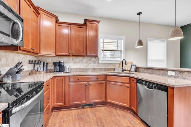 kitchen with stainless steel appliances, a peninsula, a sink, visible vents, and light wood-style floors