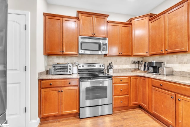 kitchen with a toaster, appliances with stainless steel finishes, brown cabinets, light wood-type flooring, and backsplash