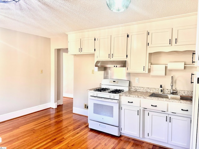 kitchen with light wood finished floors, white gas range, a sink, under cabinet range hood, and baseboards