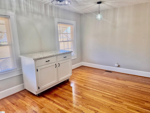 unfurnished dining area featuring light wood-type flooring, visible vents, a textured ceiling, and baseboards