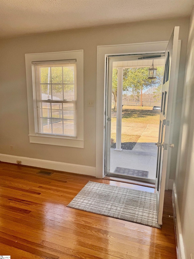 doorway to outside with baseboards, a textured ceiling, visible vents, and wood finished floors