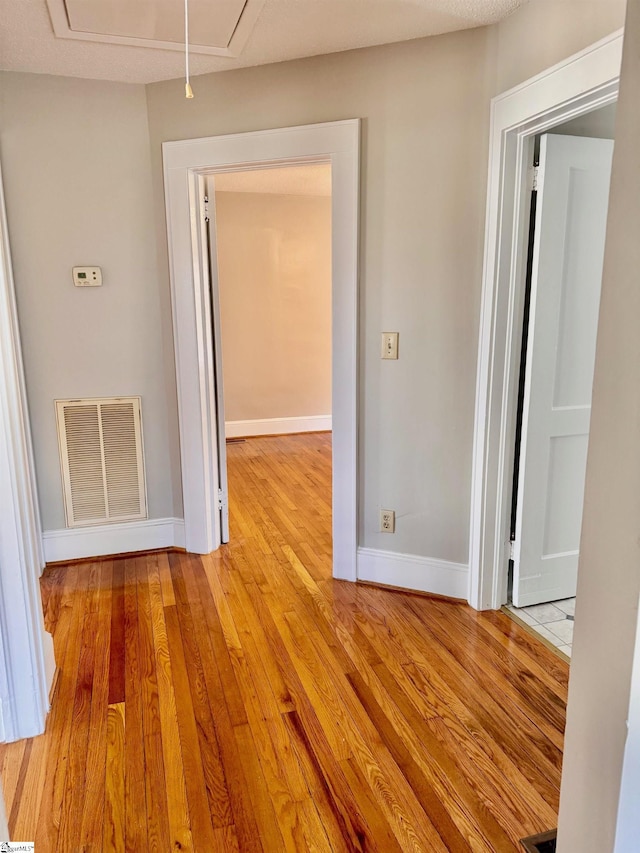 hall with light wood finished floors, attic access, visible vents, and baseboards