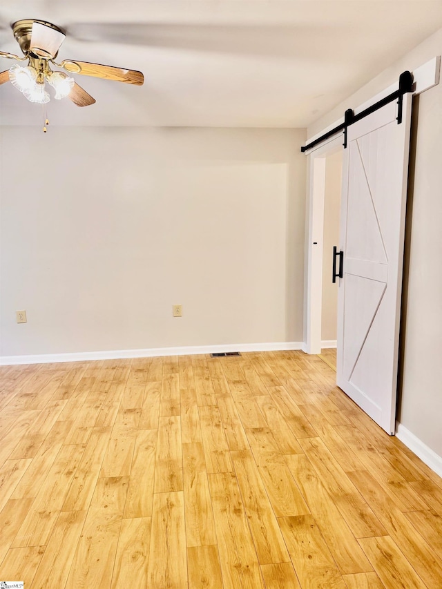 unfurnished room featuring ceiling fan, a barn door, light wood finished floors, and baseboards