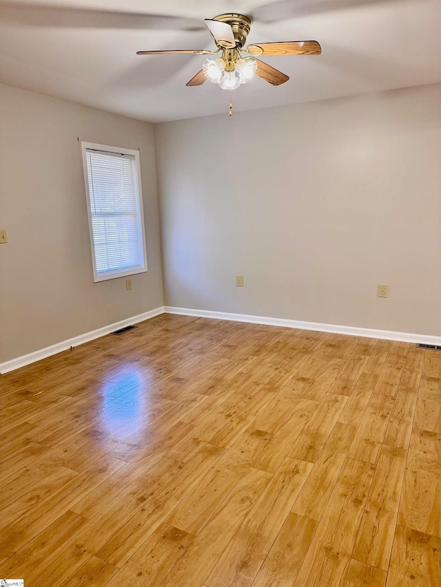 empty room with light wood finished floors, visible vents, and baseboards