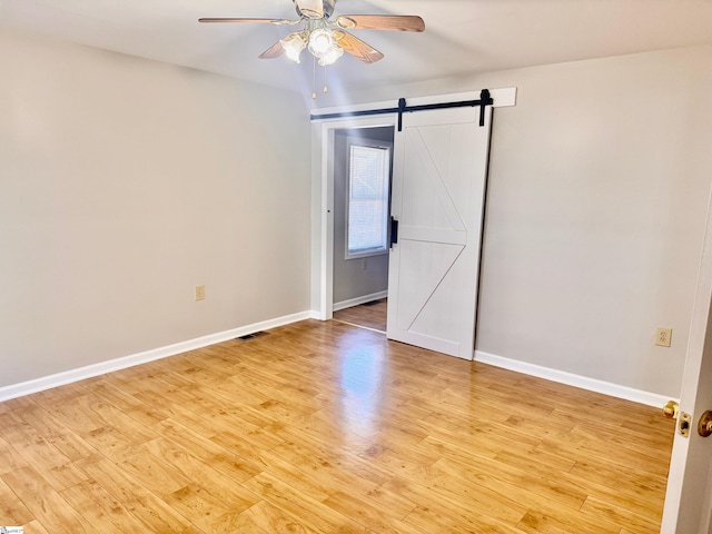 unfurnished room with ceiling fan, a barn door, baseboards, and light wood-style floors