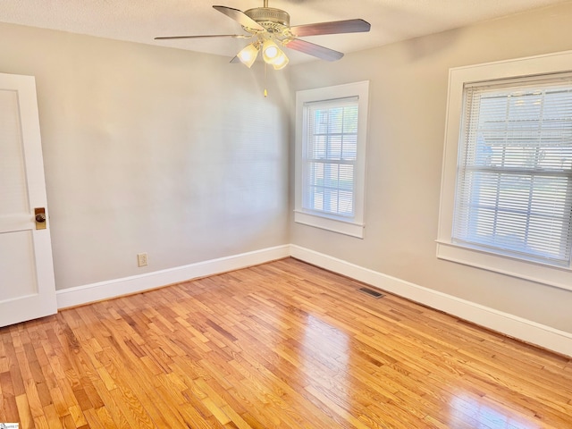 empty room with light wood-style flooring, a ceiling fan, visible vents, and baseboards