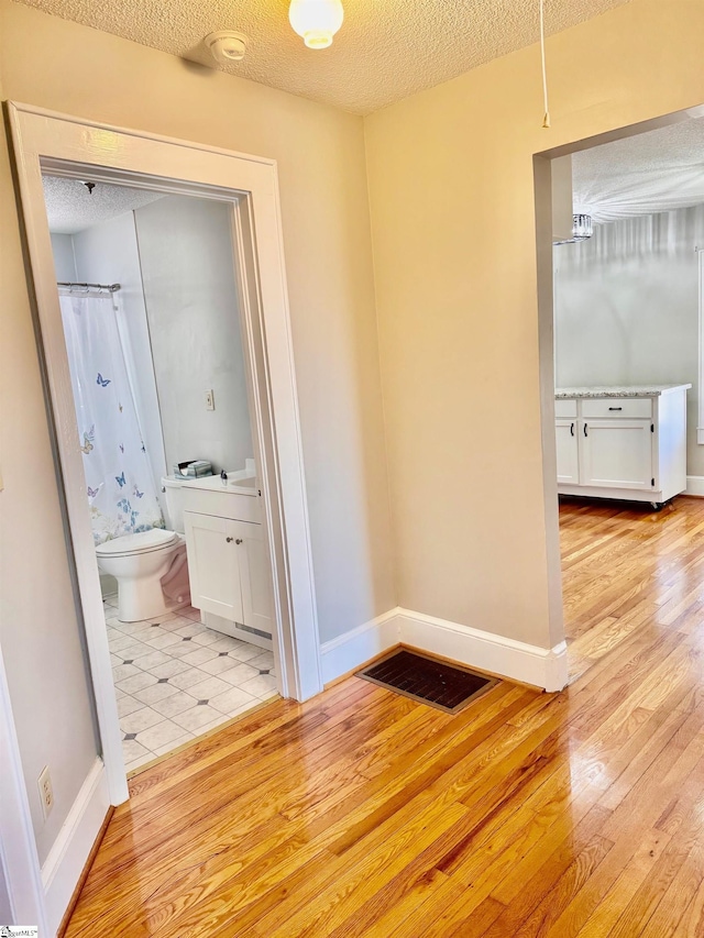 hallway with a textured ceiling, light wood finished floors, visible vents, and baseboards