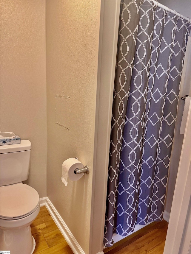 bathroom featuring toilet, baseboards, wood finished floors, and a shower with shower curtain