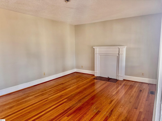 empty room featuring a textured ceiling, hardwood / wood-style flooring, and baseboards