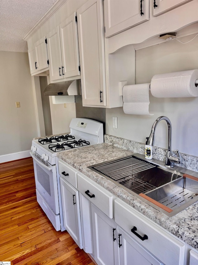 kitchen featuring white range with gas stovetop, white cabinets, light wood-style floors, under cabinet range hood, and a sink