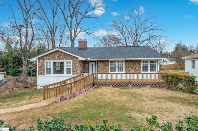 ranch-style home featuring a deck, brick siding, roof with shingles, a chimney, and a front yard