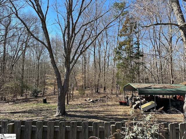 view of yard with fence, a detached carport, and a view of trees