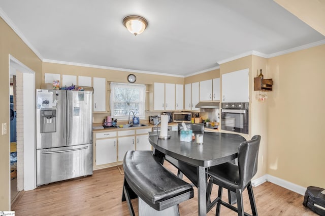 kitchen featuring stainless steel appliances, a sink, under cabinet range hood, and light wood finished floors