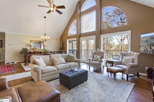 living room with high vaulted ceiling, ceiling fan with notable chandelier, baseboards, and wood finished floors