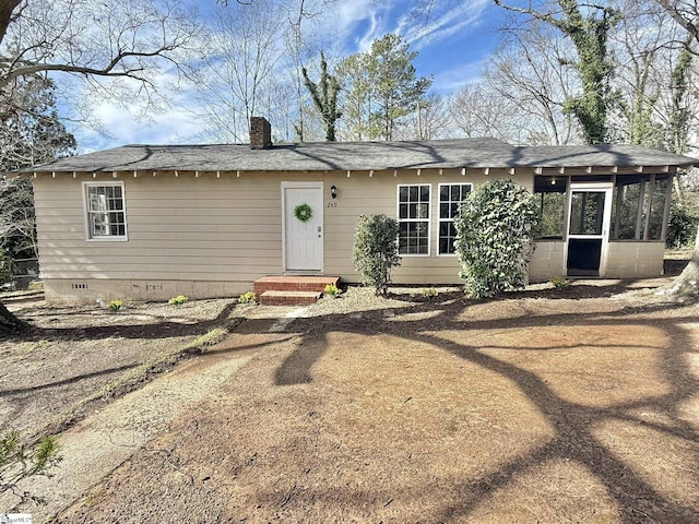 view of front of home featuring a shingled roof, crawl space, a chimney, and a sunroom