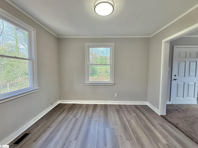 spare room featuring visible vents, crown molding, baseboards, and wood finished floors