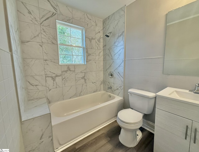 bathroom with toilet, wood finished floors, vanity, tile walls, and shower / bathing tub combination