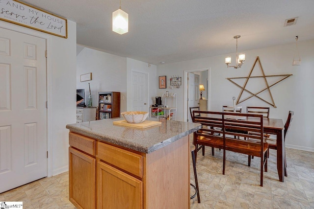 kitchen with a textured ceiling, a kitchen island, decorative light fixtures, and an inviting chandelier